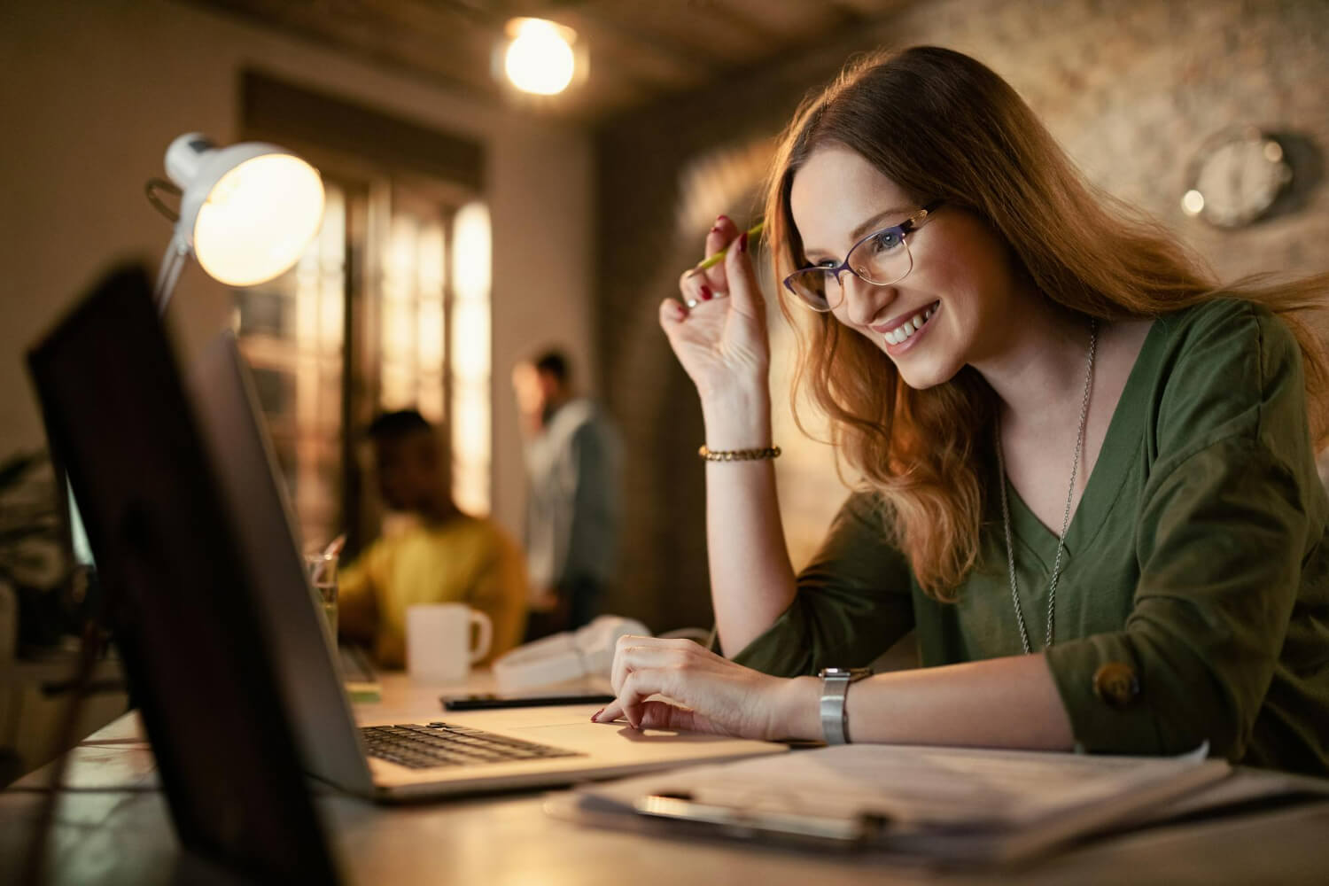 Female employee in glasses smiling at laptop