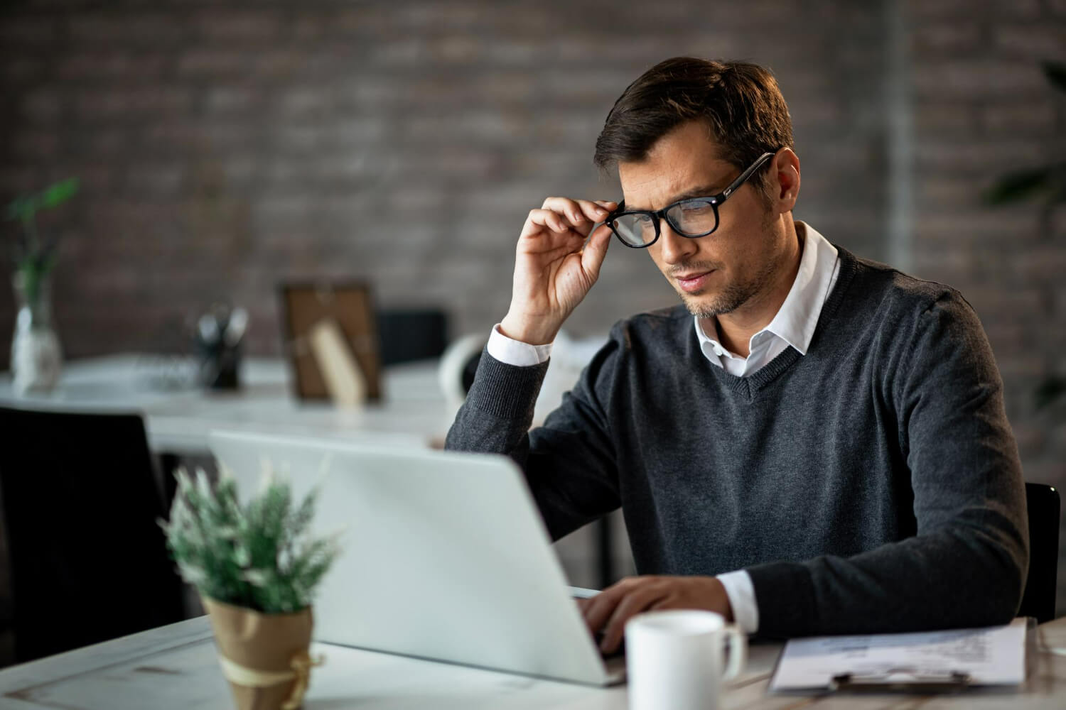 Man in glasses thinking while looking at laptop