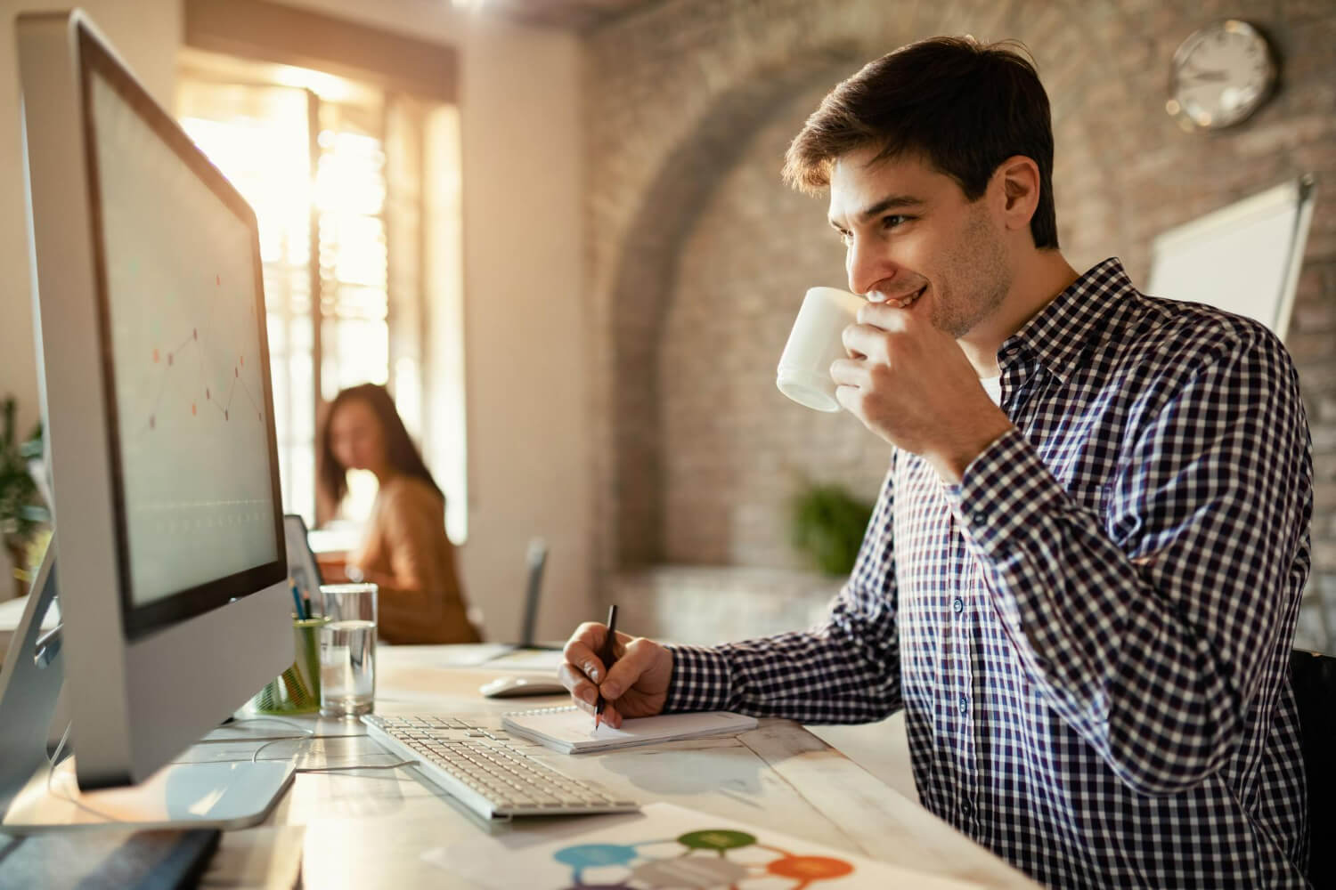 Man sipping coffee while smiling at computer